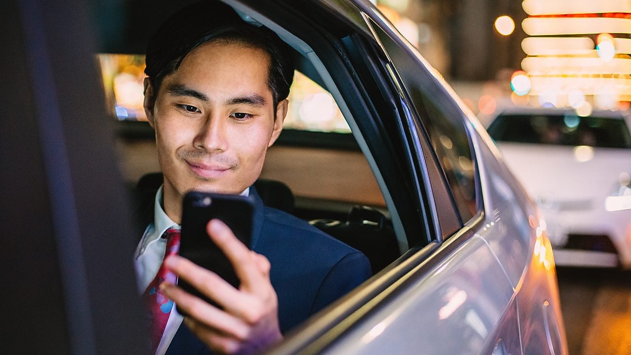 image of a man through the open backseat window of a car while he looks at his mobile device.