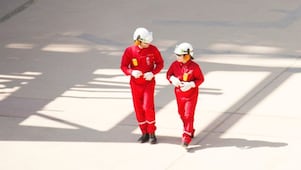 赤いオーバーオールに白いヘルメット、聴覚保護具をつけた男女の作業員が歩いている