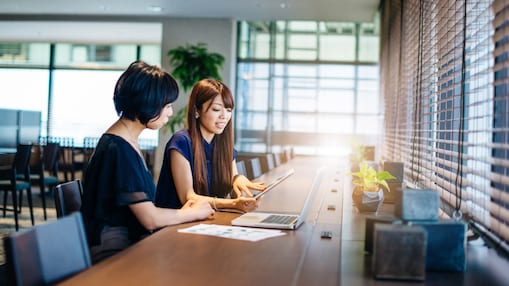 デスクに座ってコンピューターとタブレットを見つめる二人の女性